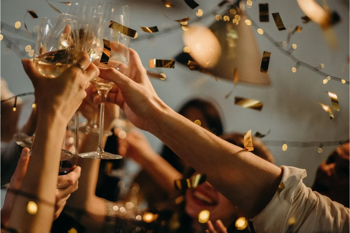 Guests raising champagne glasses in a toast as gold confetti falls at a holiday party