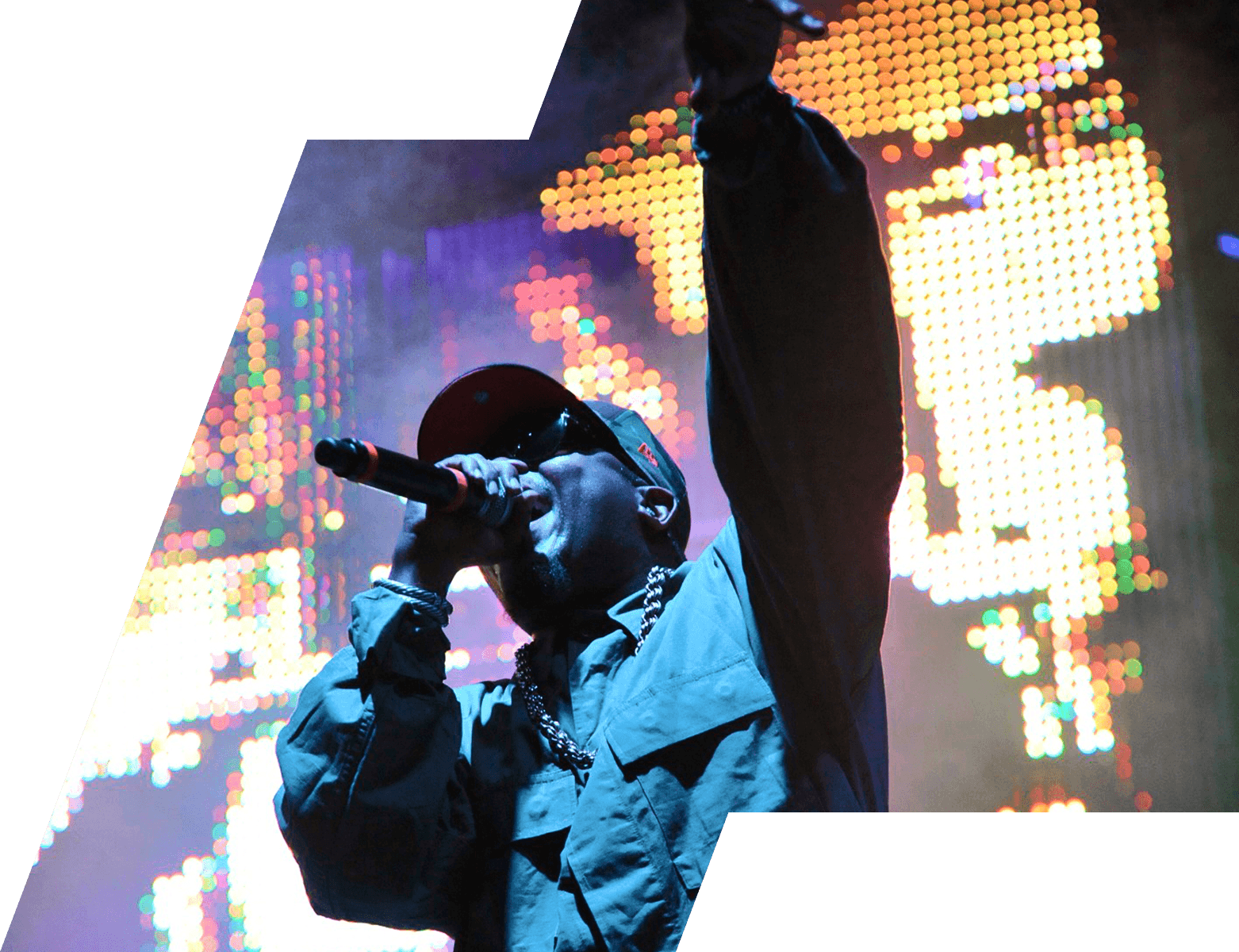 Performer raising an arm and singing into a microphone in front of a colorful pixel-style LED light wall