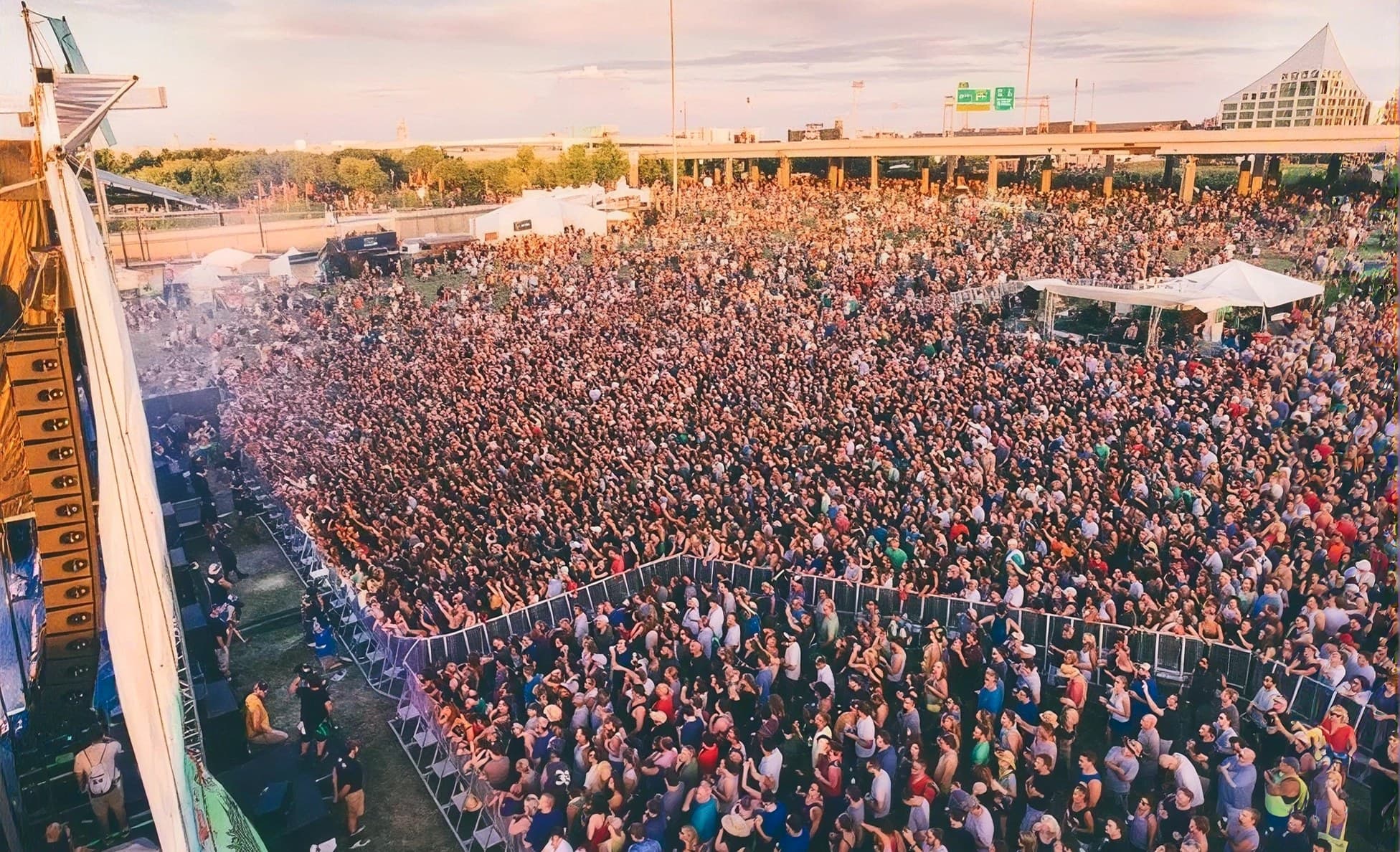 Massive festival crowd filling the grounds near an overpass at golden hour