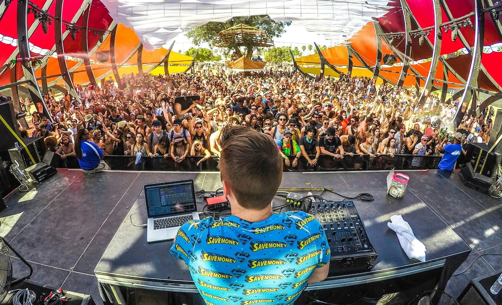 DJ performing from behind the decks to a daytime crowd under sail shades