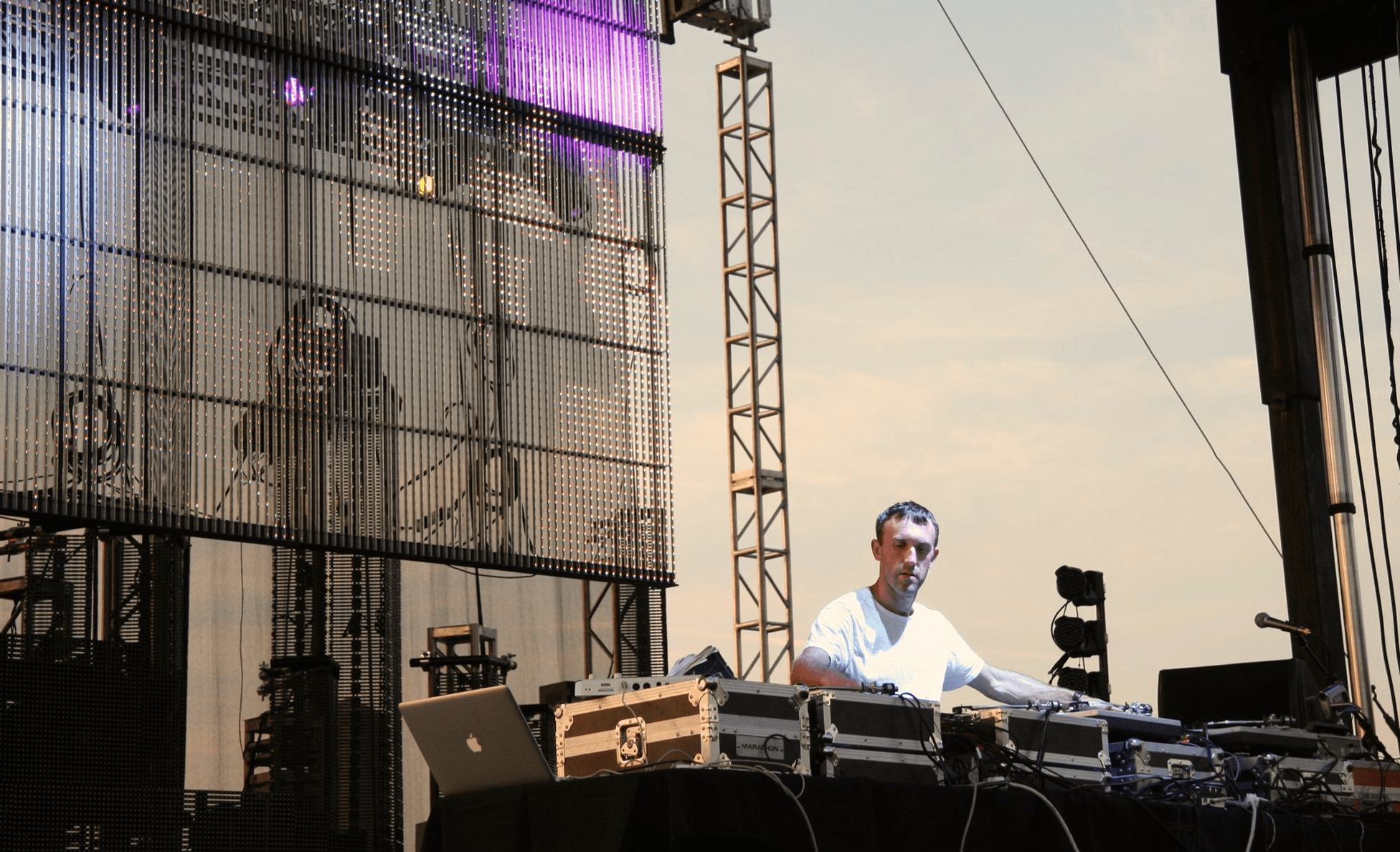 DJ performing at sunset in front of a large LED mesh screen
