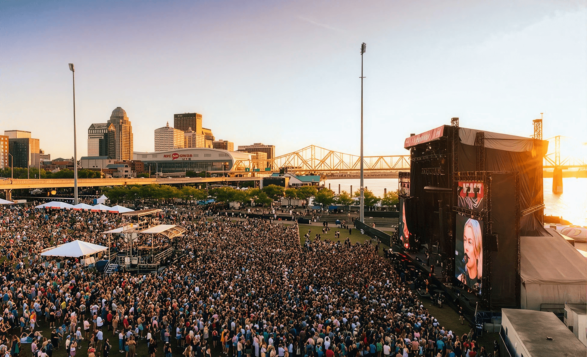 Aerial view of a riverfront festival crowd at sunset with a city skyline