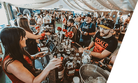Patrons being served at a festival concessions bar lined with bottles
