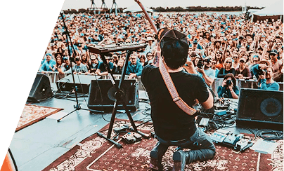 Guitarist on stage seen from behind, performing to a large festival crowd