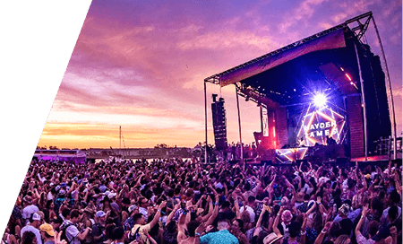Packed festival crowd facing a main stage under a purple sunset sky