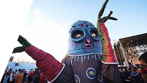 Large colorful festival puppet character with arms raised in a crowd