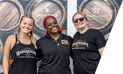 Three festival staff members in branded tees in front of bourbon barrels