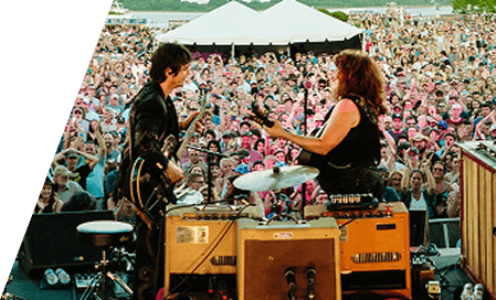 Two guitarists facing each other on a festival side stage above the crowd