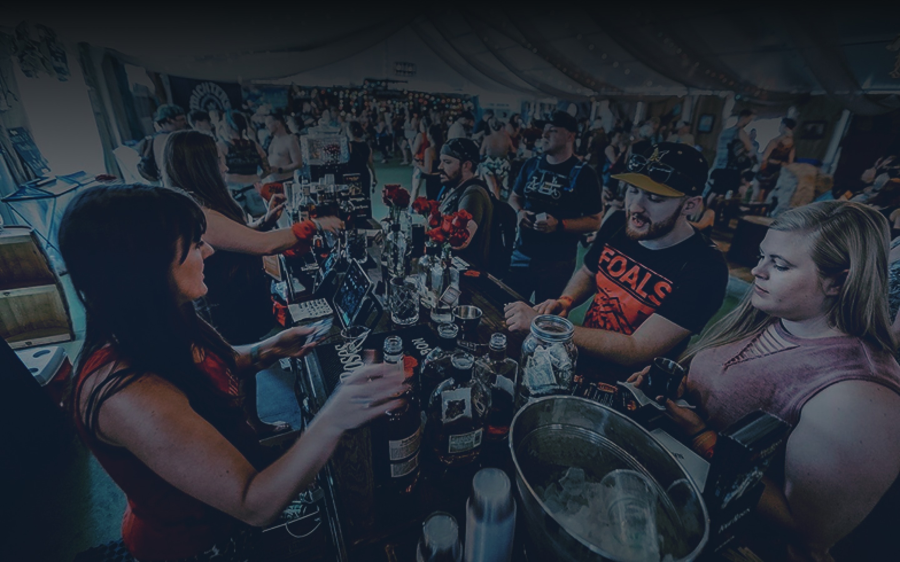 Bartenders serving cocktails to guests across a crowded festival bar tent