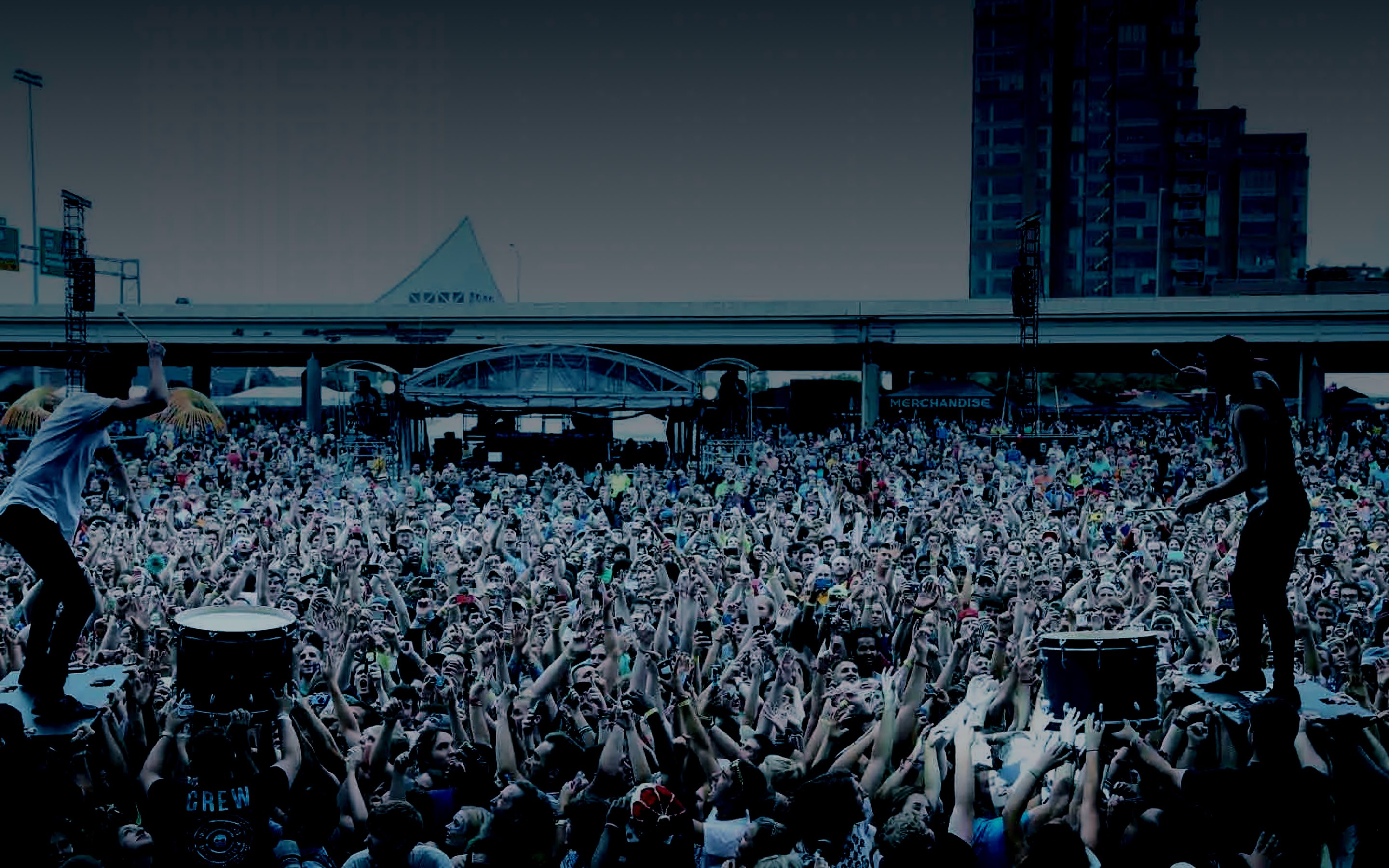 Festival crowd with raised hands in front of a main stage at dusk