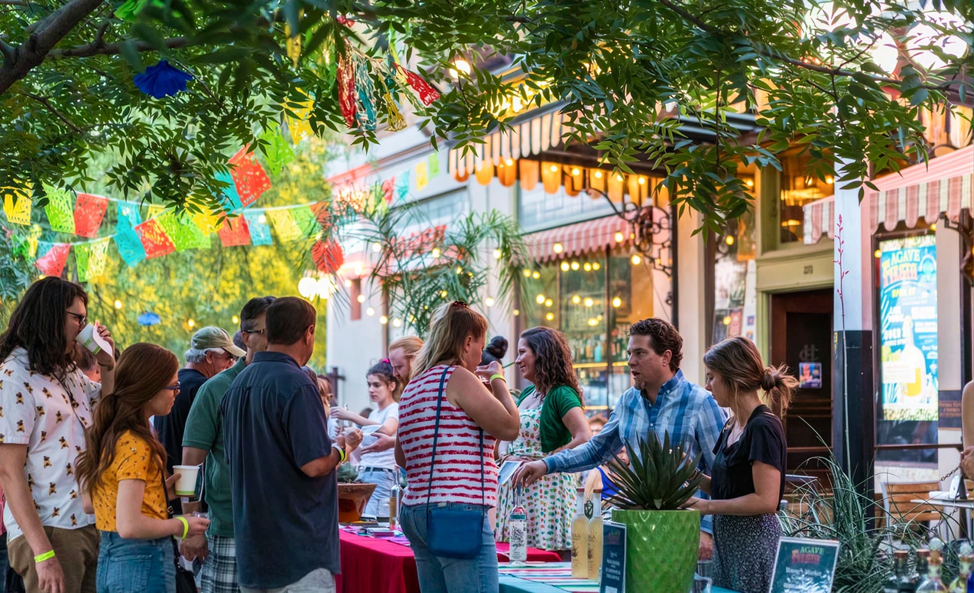 Evening agave tasting gathering under trees strung with colorful papel picado banners and string lights