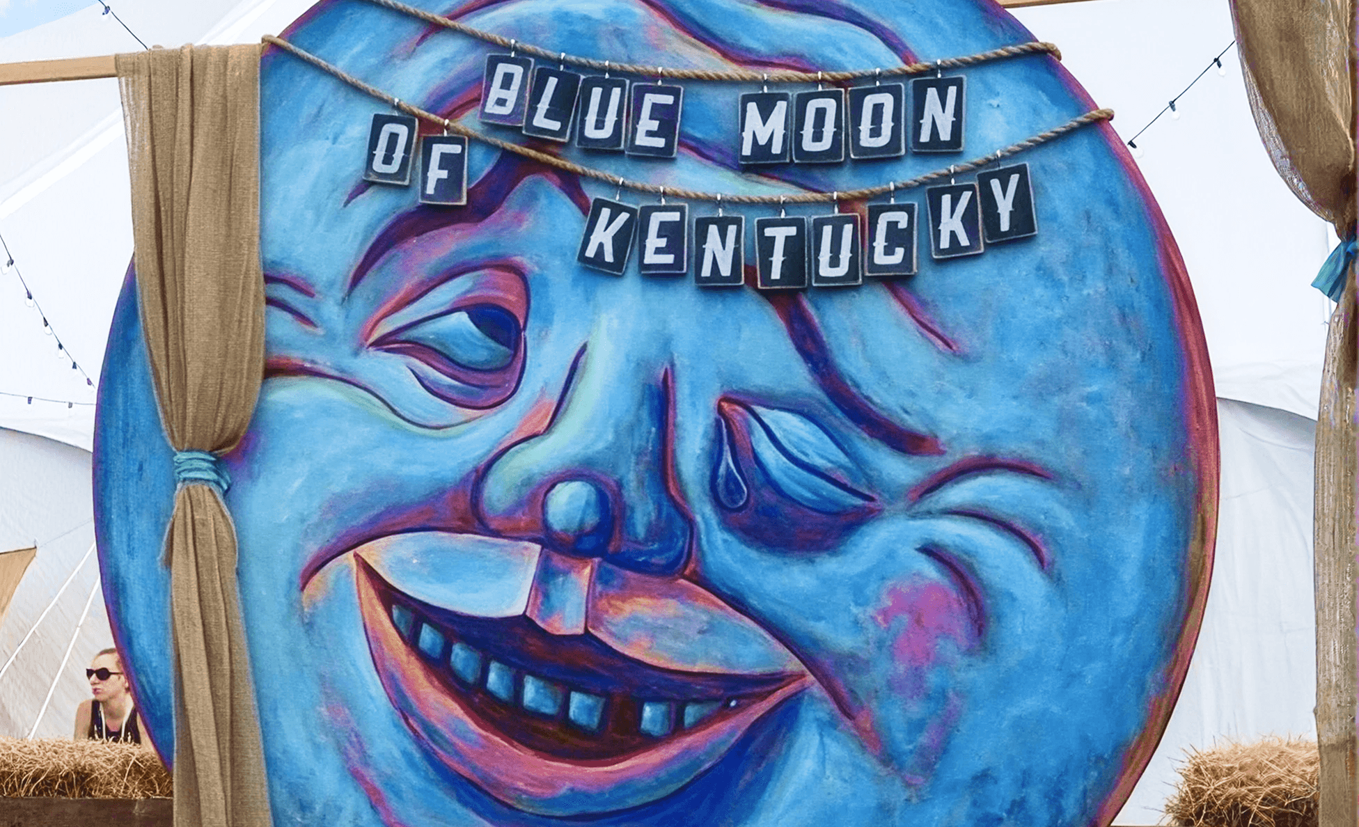Large hand-painted Blue Moon of Kentucky moon-face art installation with string lights