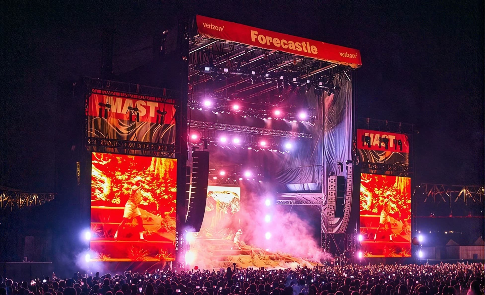 Night view of the red-lit Forecastle main stage with large video screens and a phones-up crowd