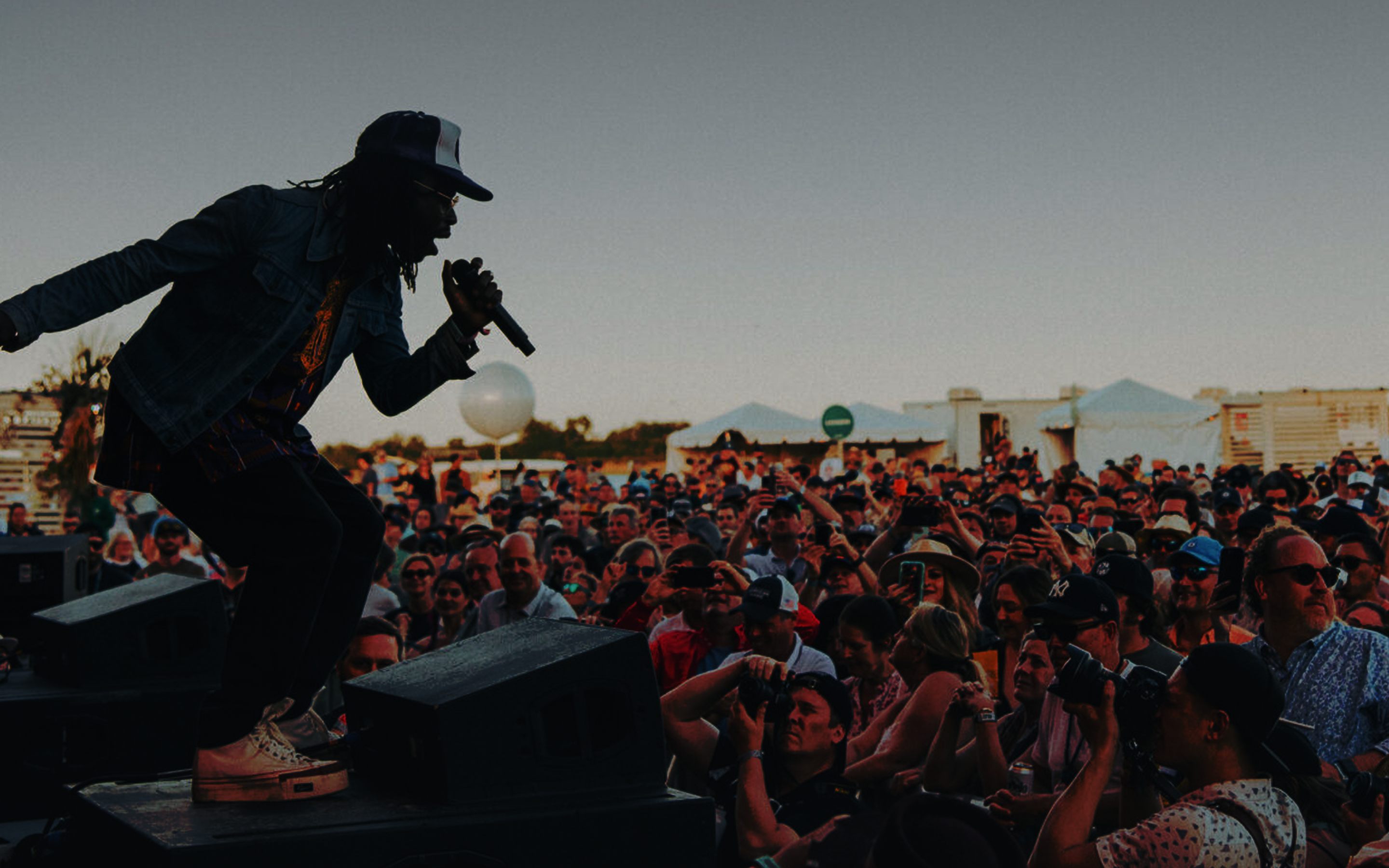 Festival performer silhouetted on stage monitors singing to a large crowd at dusk