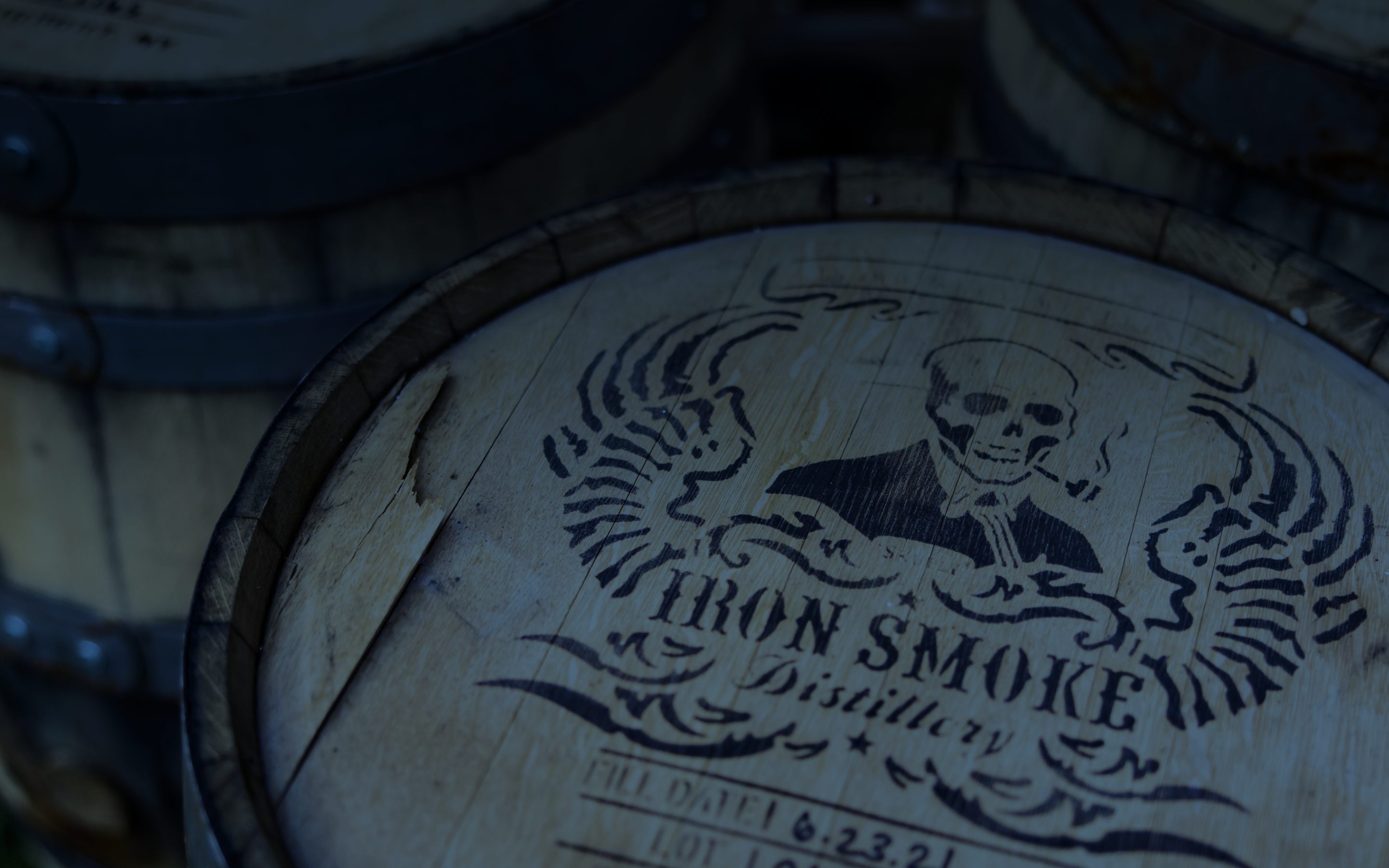 Iron Smoke Distillery whiskey barrels stacked in a dimly lit rickhouse, branded with a skull-and-wings stencil