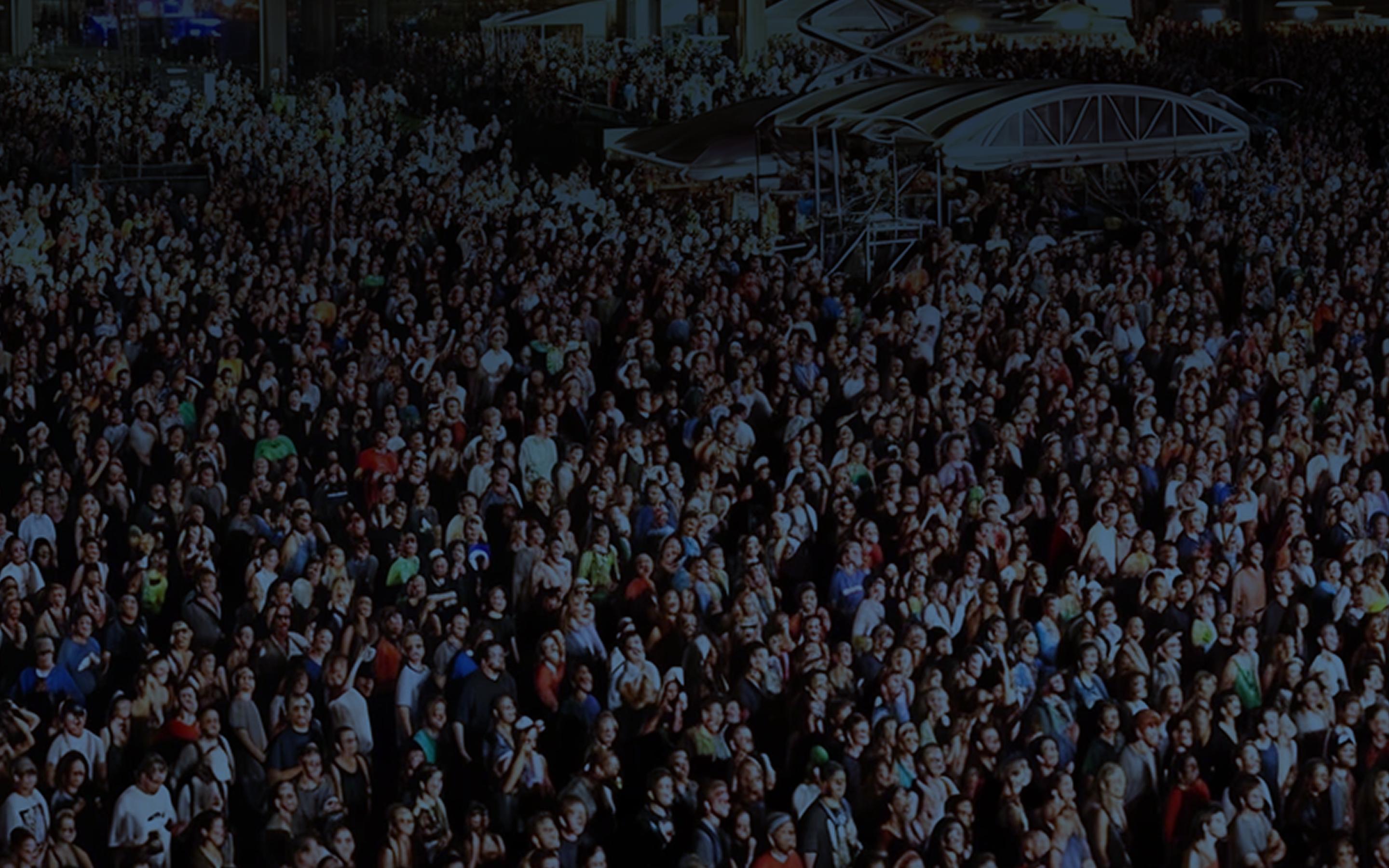 Aerial view of a massive festival crowd facing the main stage at dusk