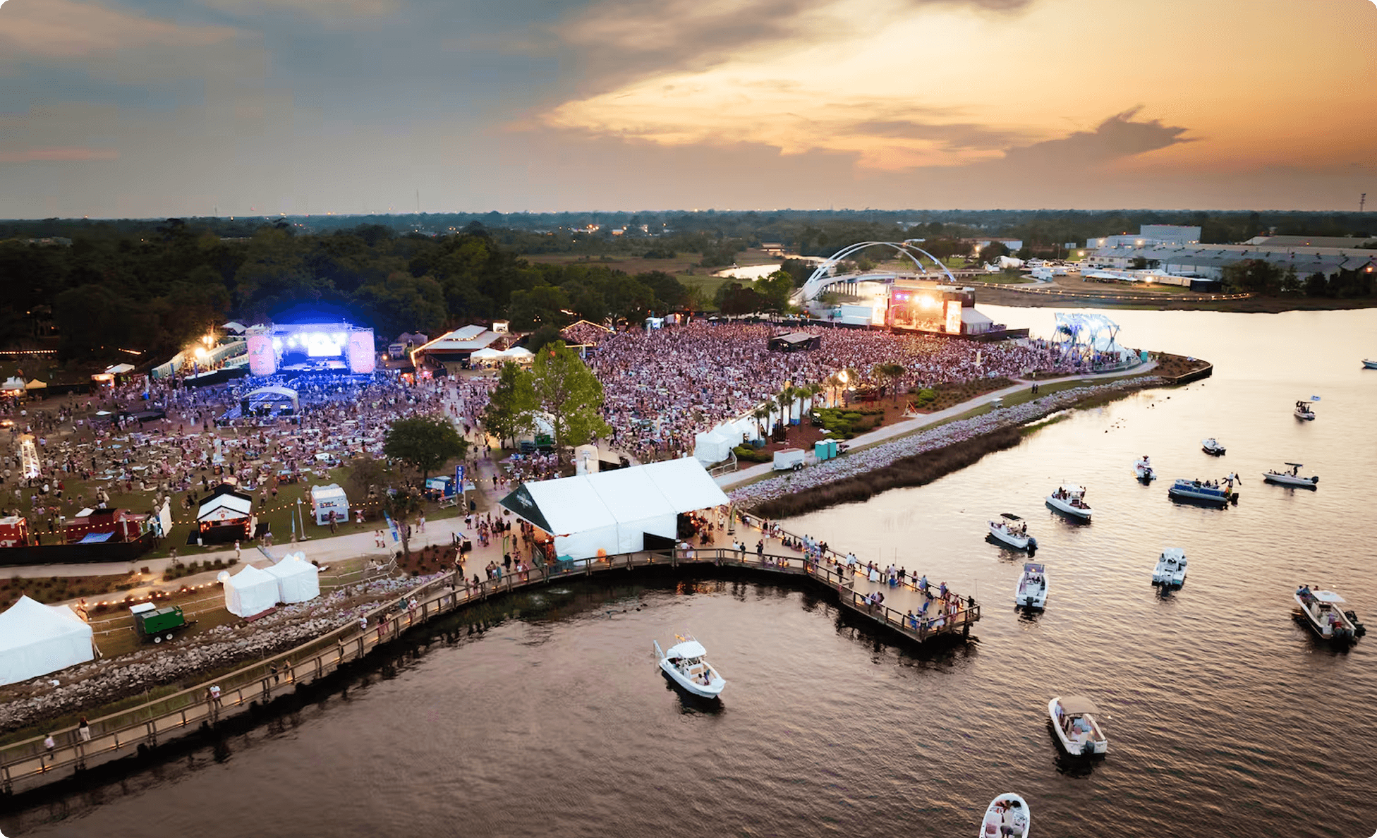 Aerial view of a waterfront festival at dusk with boats along the shoreline