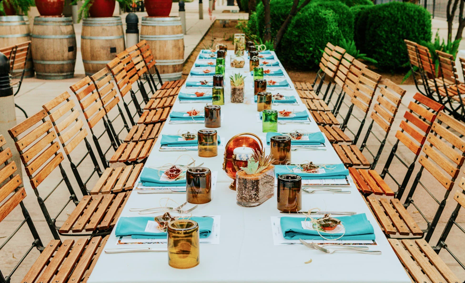 Long farm-to-table dinner setup with teal napkins among wine barrels