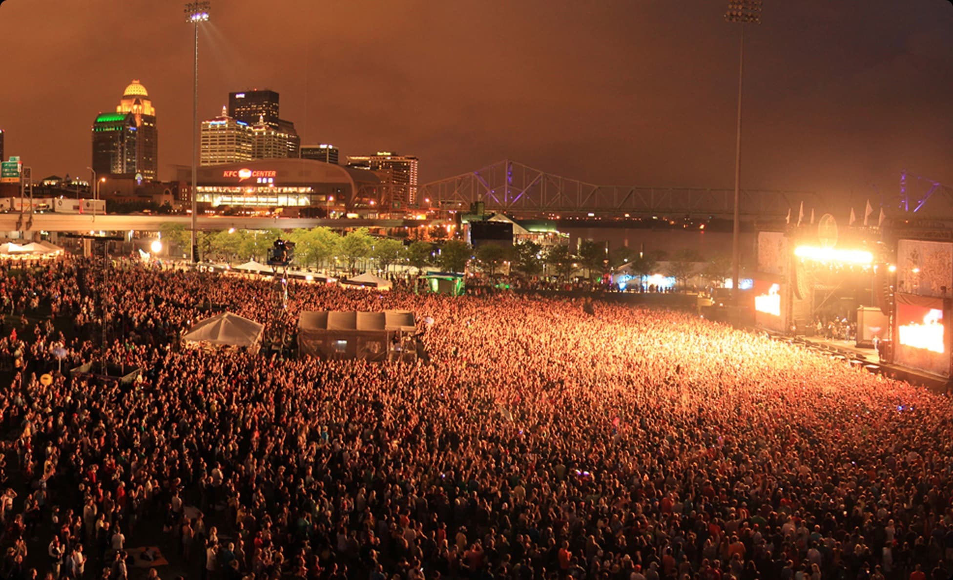 Glowing nighttime festival crowd beneath a city skyline