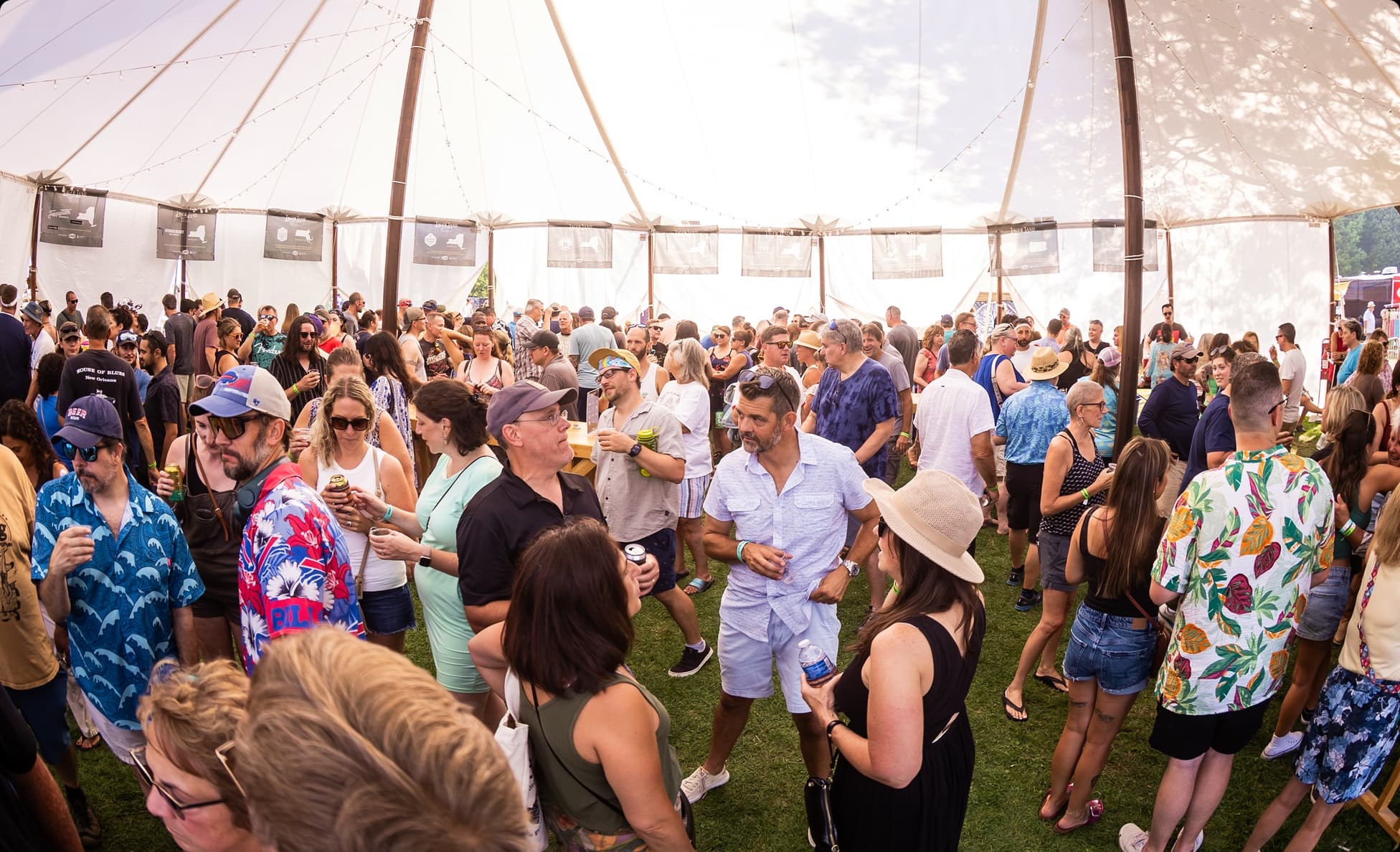 Festival-goers in tropical shirts mingling under a large sailcloth tent