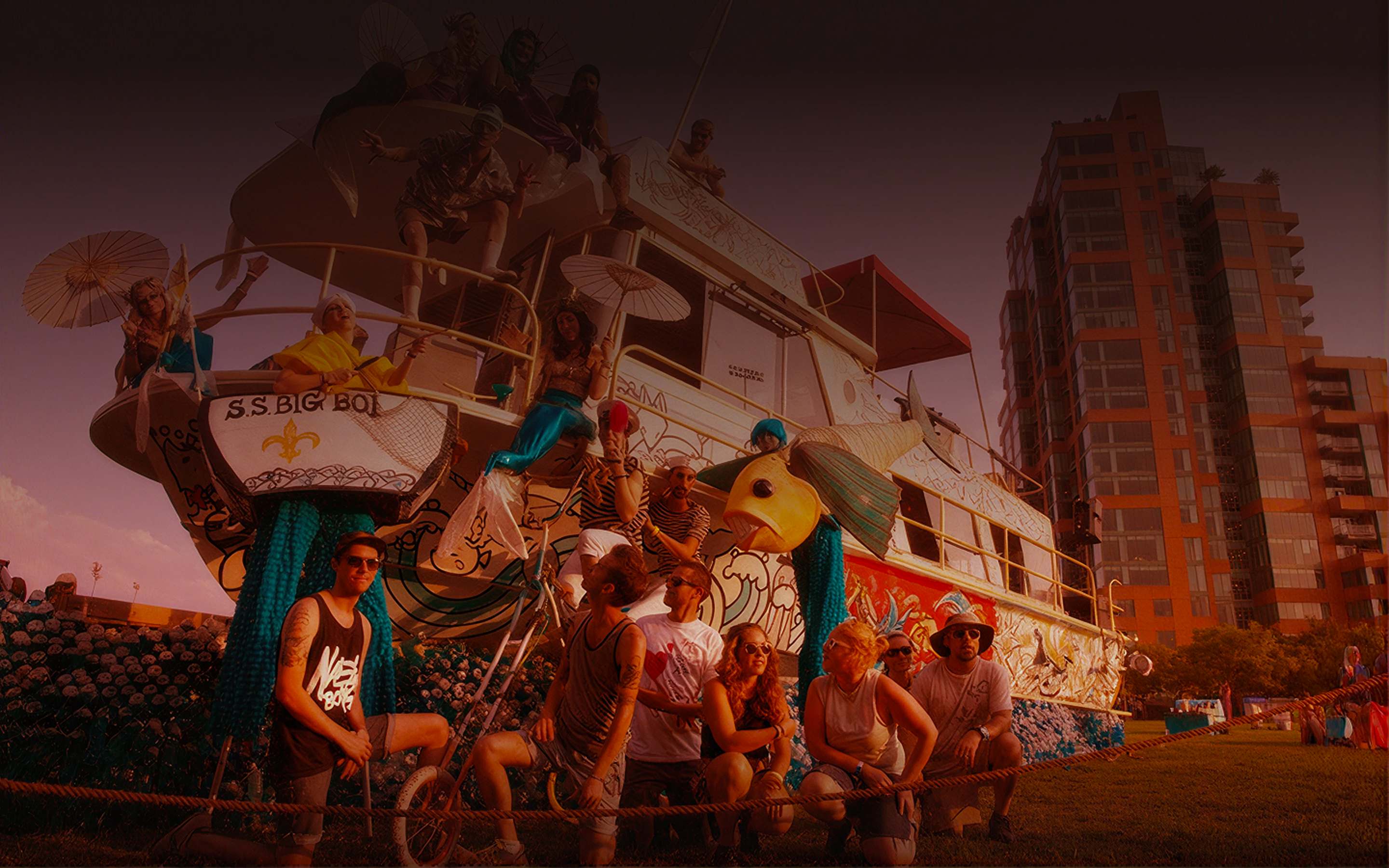 Costumed festival performers on a decorated art-boat float at golden hour with a crew posed in front