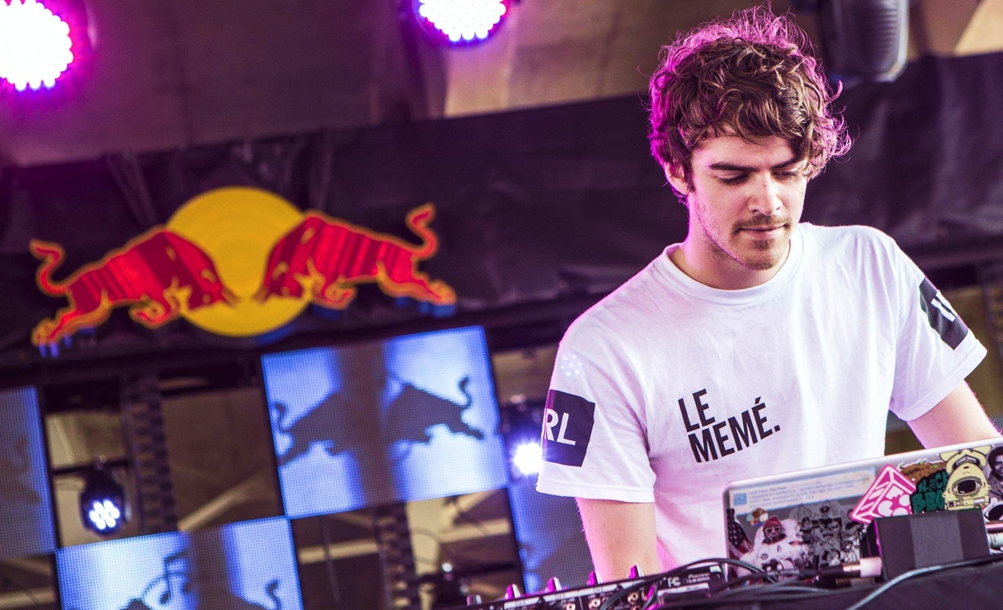 DJ in a graphic tee performing beneath a glowing Red Bull logo and LED screens